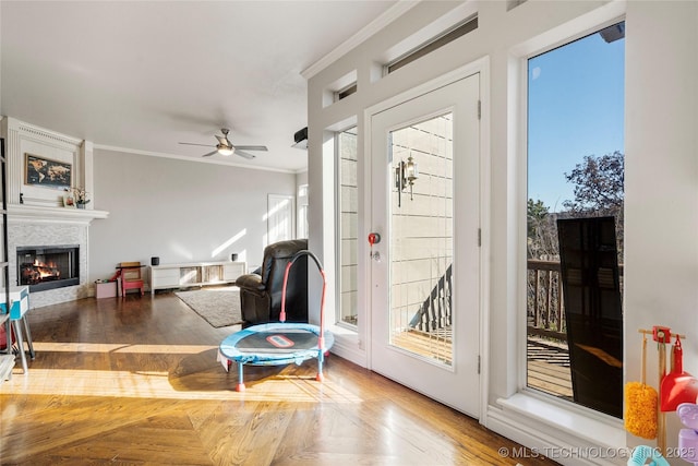 doorway with parquet floors, a glass covered fireplace, a ceiling fan, and crown molding