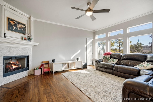 living area with a ceiling fan, a glass covered fireplace, crown molding, and wood finished floors