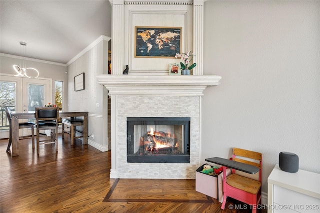 room details featuring ornamental molding, a notable chandelier, a tiled fireplace, and wood finished floors