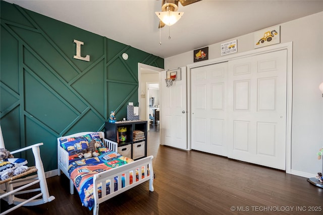 bedroom with a closet, dark wood-style flooring, a decorative wall, and baseboards