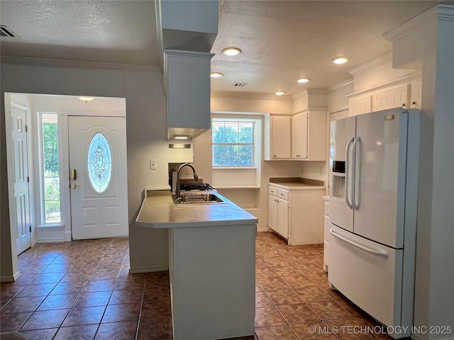 kitchen with a peninsula, a sink, white fridge with ice dispenser, white cabinetry, and crown molding