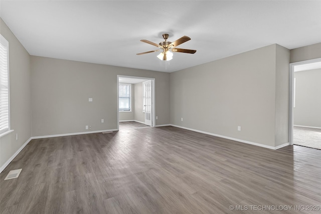 empty room featuring a ceiling fan, visible vents, baseboards, and wood finished floors