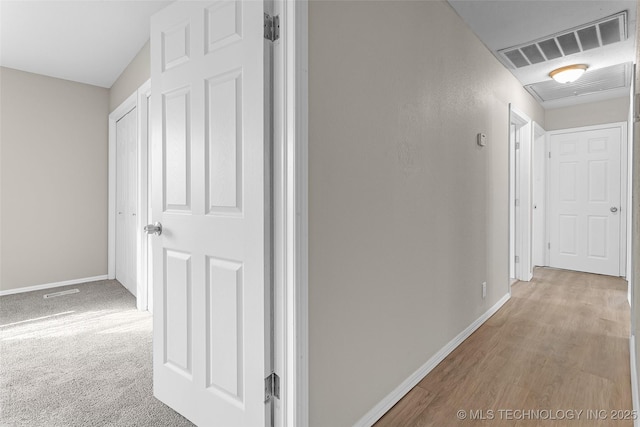 corridor featuring carpet, wood finished floors, visible vents, and baseboards