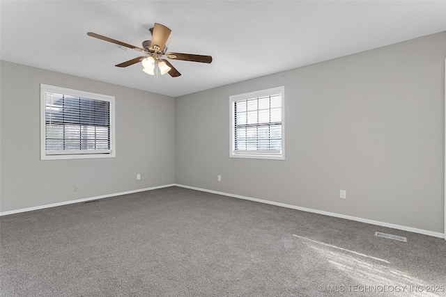 spare room with ceiling fan, dark carpet, visible vents, and baseboards