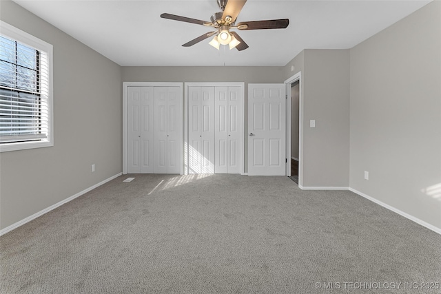 unfurnished bedroom featuring a ceiling fan, carpet, baseboards, and two closets