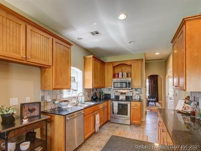 kitchen featuring arched walkways, stainless steel appliances, dark countertops, visible vents, and a sink