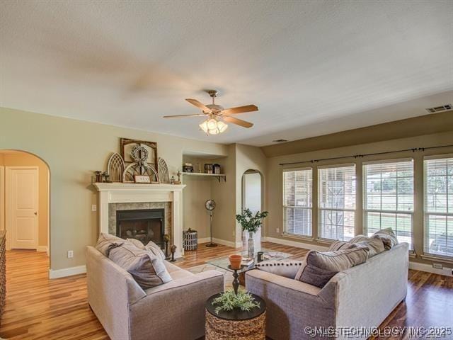 living room with baseboards, visible vents, arched walkways, wood finished floors, and a fireplace