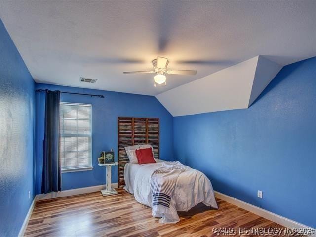 bedroom featuring lofted ceiling, visible vents, baseboards, and wood finished floors