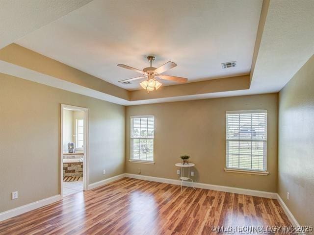 unfurnished room featuring a tray ceiling, visible vents, ceiling fan, wood finished floors, and baseboards