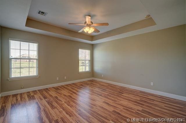 spare room with baseboards, visible vents, a ceiling fan, wood finished floors, and a tray ceiling