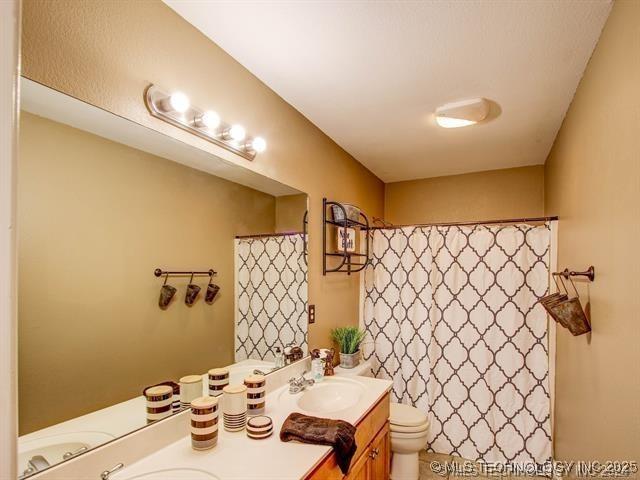 bathroom with curtained shower, a sink, toilet, and double vanity