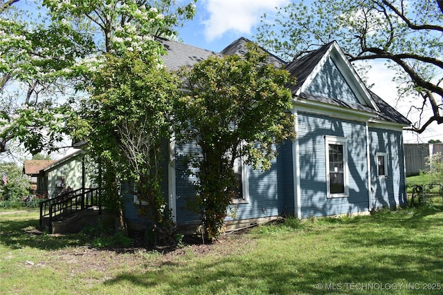 view of side of home with roof with shingles and a lawn