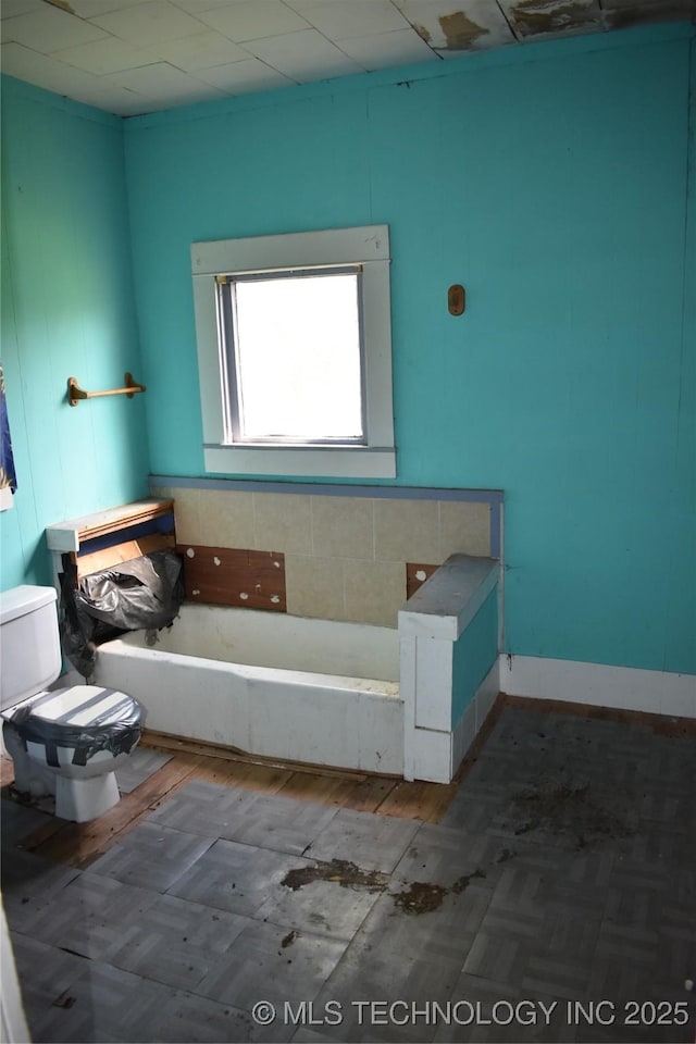 bathroom with parquet flooring, a garden tub, and toilet