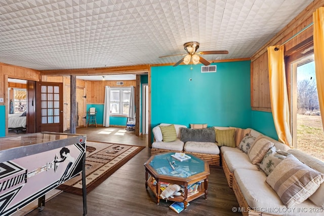 living room with a ceiling fan, wooden walls, wood finished floors, and visible vents