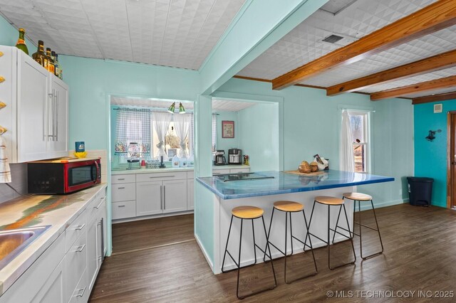 kitchen featuring beamed ceiling, a kitchen breakfast bar, white cabinets, and dark wood finished floors