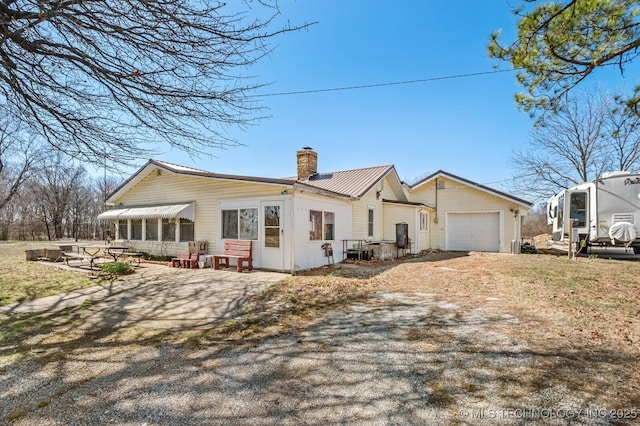 view of front of house featuring dirt driveway, metal roof, a chimney, an attached garage, and a patio