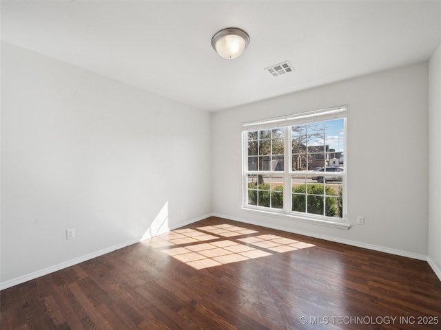 empty room with wood finished floors, visible vents, and baseboards