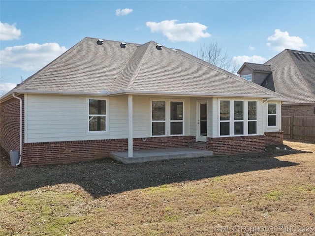 rear view of house featuring brick siding, a shingled roof, a lawn, a patio area, and fence