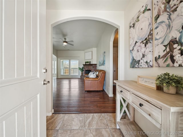 foyer entrance featuring a ceiling fan, arched walkways, and a brick fireplace