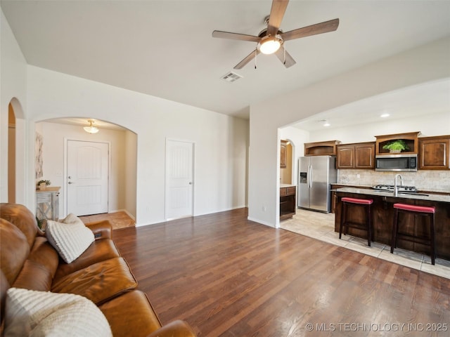 living room with light wood finished floors, ceiling fan, visible vents, and arched walkways