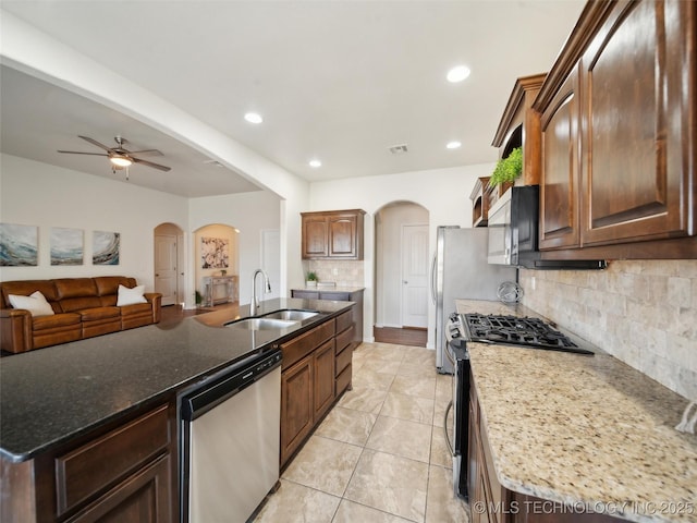 kitchen featuring arched walkways, stainless steel appliances, a ceiling fan, open floor plan, and a sink