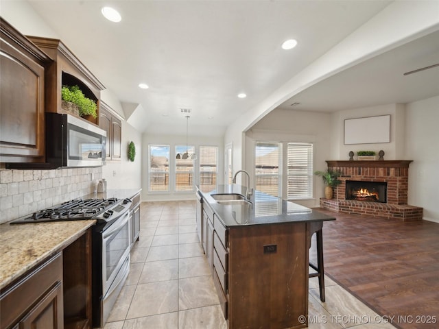 kitchen with backsplash, appliances with stainless steel finishes, a brick fireplace, a sink, and a kitchen breakfast bar