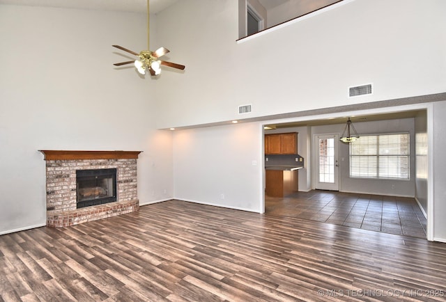 unfurnished living room featuring a brick fireplace, visible vents, dark wood finished floors, and baseboards