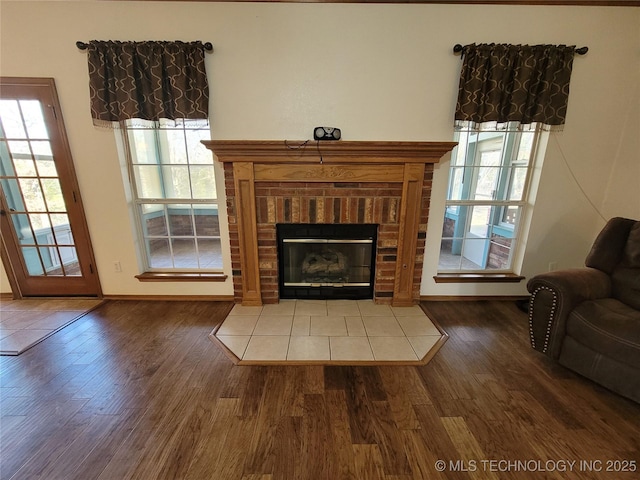 living room featuring a brick fireplace, baseboards, and wood finished floors