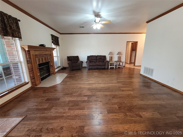 living area with ornamental molding, a brick fireplace, wood finished floors, and visible vents