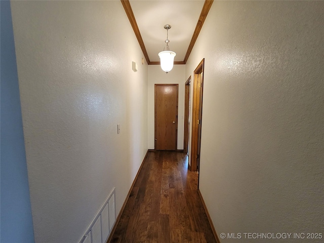 corridor featuring a textured wall, dark wood-type flooring, visible vents, baseboards, and crown molding