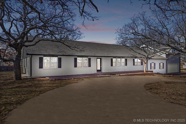 ranch-style home with brick siding, driveway, an attached garage, and roof with shingles