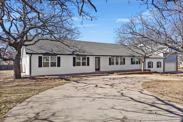 ranch-style house featuring brick siding, driveway, and roof with shingles