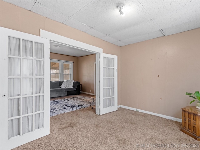 carpeted spare room featuring french doors, a drop ceiling, and baseboards