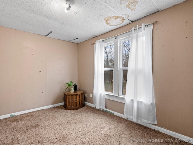 carpeted empty room featuring a drop ceiling and baseboards