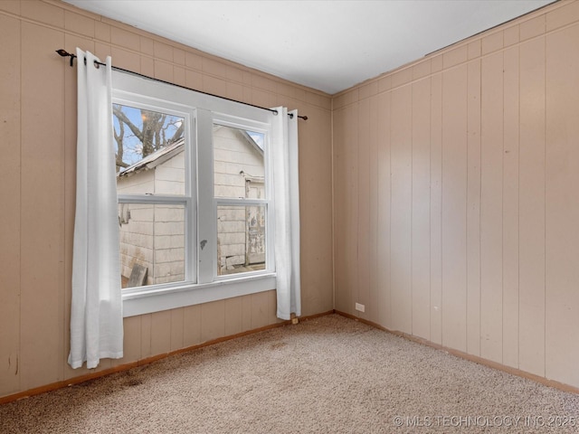 carpeted spare room featuring wood walls and baseboards