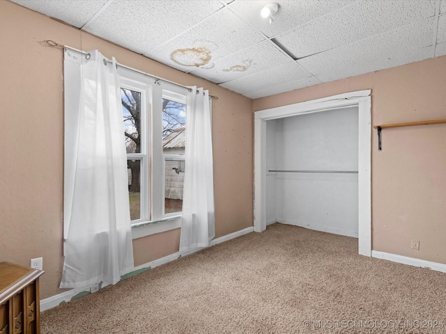 unfurnished bedroom with a closet, a drop ceiling, carpet flooring, and baseboards