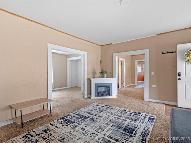 living room with baseboards, carpet flooring, crown molding, and a glass covered fireplace