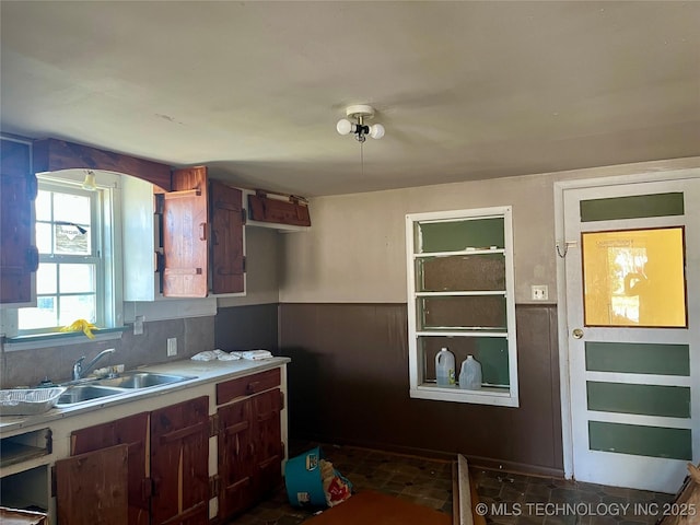 kitchen with decorative backsplash, light countertops, a wainscoted wall, and a sink