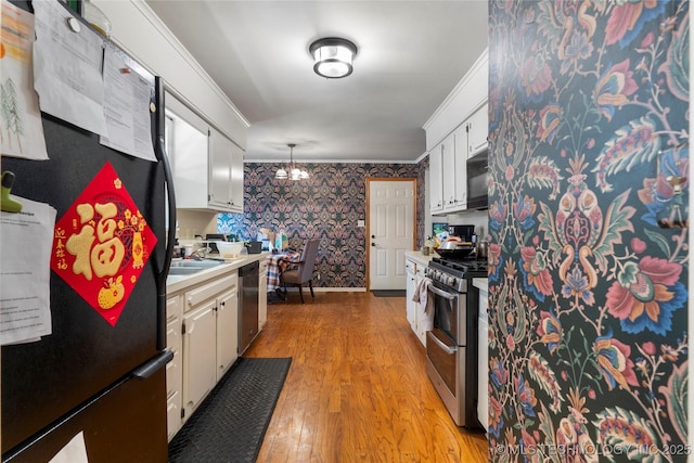 kitchen with light countertops, ornamental molding, light wood-type flooring, black appliances, and wallpapered walls