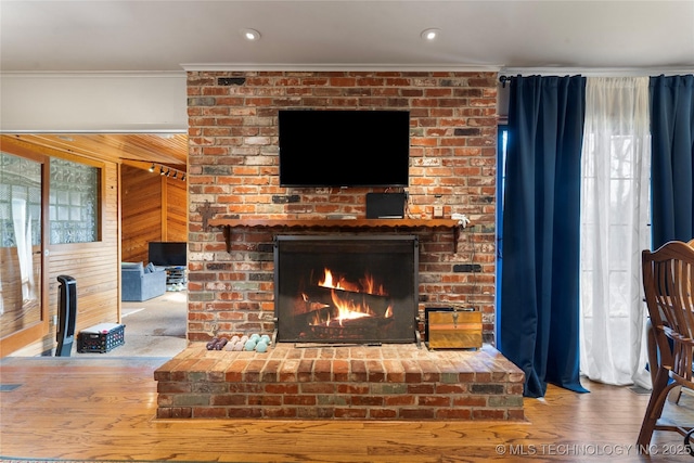 living room with a fireplace, visible vents, ornamental molding, wooden walls, and wood finished floors