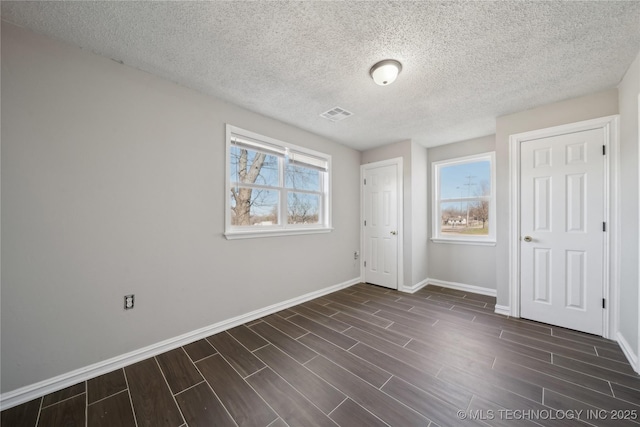 unfurnished bedroom featuring a textured ceiling, visible vents, baseboards, and wood tiled floor