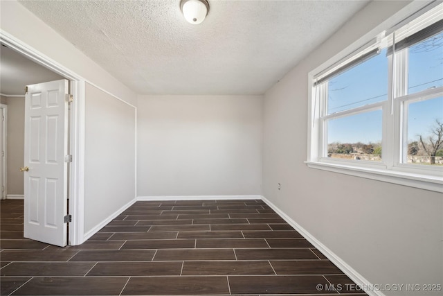 unfurnished room with a textured ceiling, baseboards, and wood tiled floor