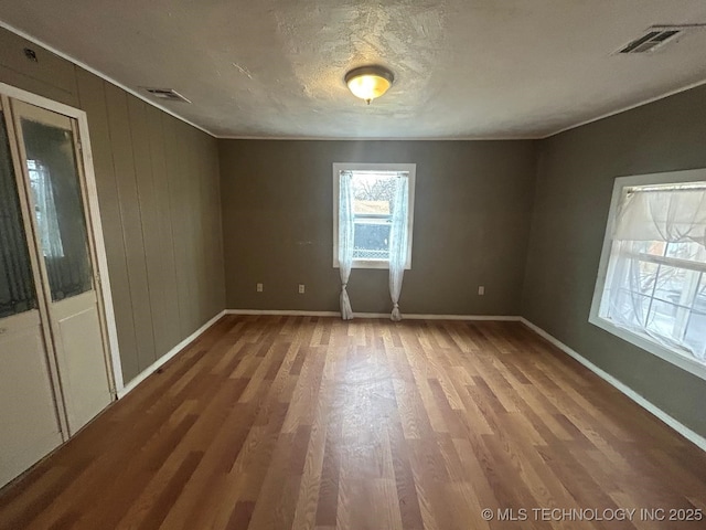 empty room featuring visible vents, a textured ceiling, baseboards, and wood finished floors