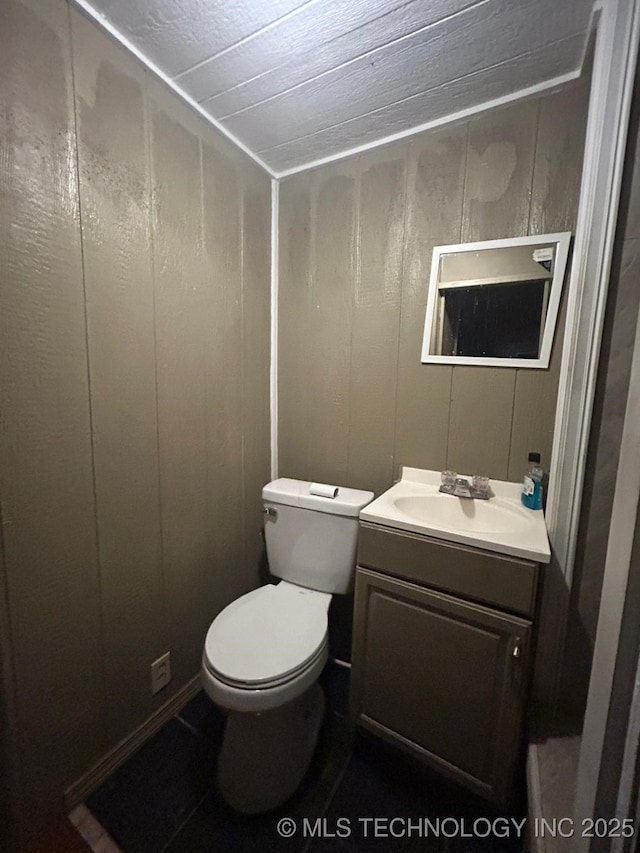 bathroom with wooden walls, a decorative wall, vanity, and toilet