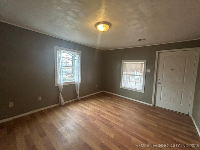 empty room with a textured ceiling, wood finished floors, visible vents, and baseboards