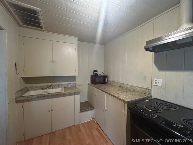 kitchen with black range with electric cooktop, a sink, visible vents, light countertops, and light wood finished floors