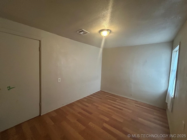 unfurnished room with a textured ceiling, wood finished floors, and visible vents