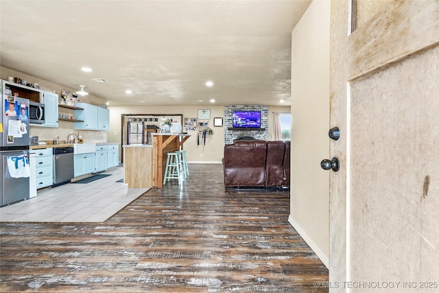 kitchen featuring a breakfast bar, open shelves, appliances with stainless steel finishes, open floor plan, and wood finished floors