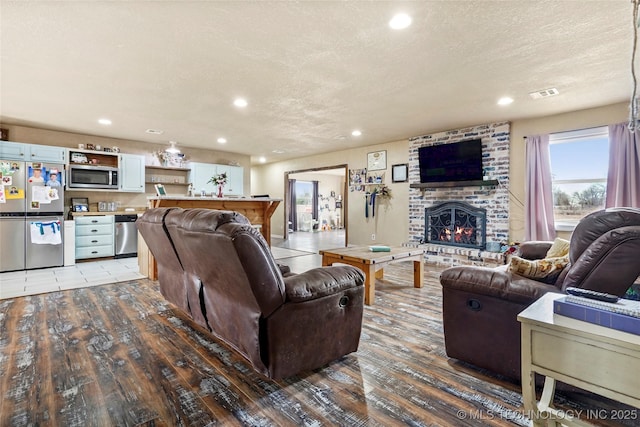 living room featuring a brick fireplace, visible vents, a textured ceiling, and wood finished floors