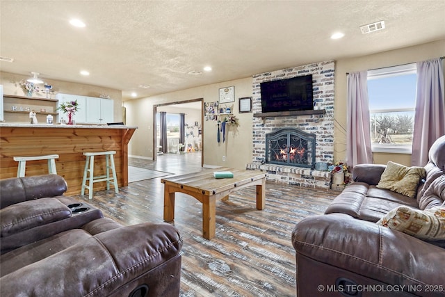 living area featuring a brick fireplace, a textured ceiling, visible vents, and wood finished floors